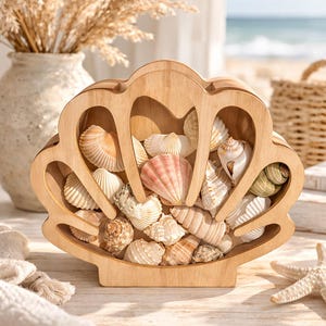 Peut inclure: Un présentoir en bois en forme de coquillage rempli de divers coquillages. Le présentoir est en bois de couleur claire et a un bord festonné. Les coquillages sont dans les tons de blanc, rose et marron. Une étoile de mer est sur la table.