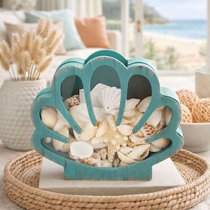 Könnte beinhalten: Eine türkisfarbene, muschelförmige Holz-Dekobox, gefüllt mit verschiedenen Muscheln und einem Seestern. Die Box steht auf einem geflochtenen Tablett und schafft ein Küsten-Thema. Die Box ist mit weißen, beigen und braunen Muscheln gefüllt.