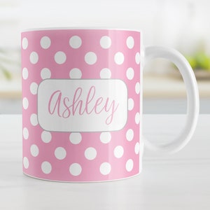 May include: A pink ceramic mug with white polka dots and the name "Ashley" in a gray rectangle.