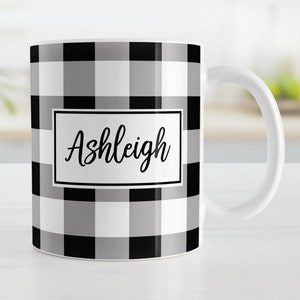 May include: White ceramic mug with a black and gray buffalo plaid pattern. The mug has a black border around the name "Ashleigh" in a white rectangle.