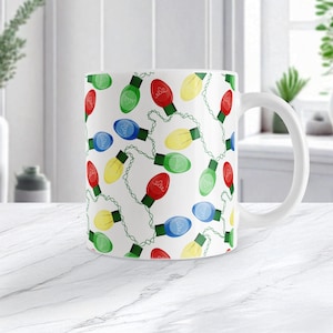 May include: White ceramic mug featuring a repeating pattern of colorful Christmas lights. The lights are red, green, blue, and yellow, strung together with green wire. The mug has a white handle and a glossy finish.