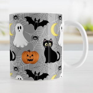 May include: A white ceramic mug with a Halloween themed design. The mug features a repeating pattern of black cats, bats, ghosts, pumpkins, and spiders on a gray background with white spiderwebs.