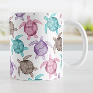 May include: White ceramic mug featuring a repeating pattern of colorful sea turtles. The turtles are in shades of pink, purple, teal, and brown, with floral designs on their shells. The mug has a white handle and a glossy finish.