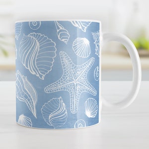 May include: A white ceramic mug with a blue background and a white pattern of seashells and starfish.