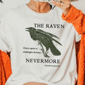 May include: White t-shirt with a black raven illustration and the text "THE RAVEN" and "NEVERMORE" with the author Edgar Allen Poe's name below.