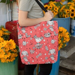 May include: Red tote bag with a repeating pattern of knitting-themed illustrations. The design includes cartoon figures, yarn balls, knitting needles, and socks. The bag has a black strap and is being held in front of a flower shop.