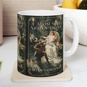 May include: White ceramic mug with a green, black, and gold design featuring an illustration of a fairy and a man playing a lute. The text "A Midsummer Night's Dream" and "William Shakespeare" are printed on the mug.
