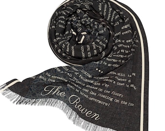 Può includere: Una sciarpa nera e bianca con un bordo a frangia. La sciarpa presenta una stampa del poema "Il Corvo" di Edgar Allan Poe.