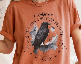 Może przedstawiać: Koszulka w kolorze rdzy z grafiką czarnego kruka i tekstem "Once upon a midnight dreary" oraz "Edgar Allan Poe" w stylu vintage.