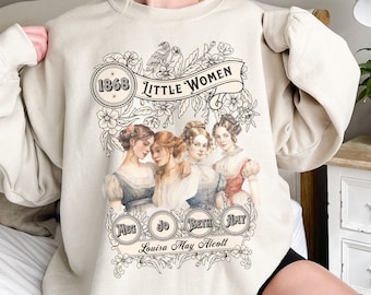 Könnte beinhalten: Ein beiger Pullover mit einem Vintage-inspirierten Grafikdruck der vier March-Schwestern aus dem Roman *Little Women* von Louisa May Alcott. Die Grafik zeigt die Namen der Schwestern, Meg, Jo, Beth und Amy, sowie das Jahr 1868.