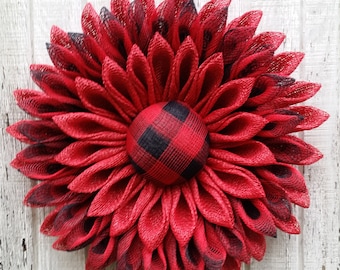 May include: A red and black plaid wreath with a large red flower in the center. The wreath is made of mesh and is decorated with a black and red plaid bow.