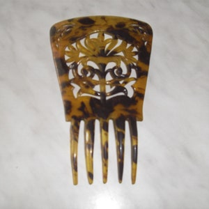 May include: A brown and black tortoiseshell hair comb with a decorative cutout design. The comb has five tines.