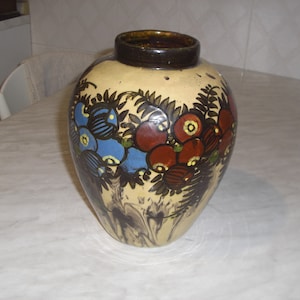 Puede incluir: Un jarrón de cerámica con cuerpo de color crema y borde marrón. El jarrón está decorado con un patrón floral en tonos azules, rojos y verdes.