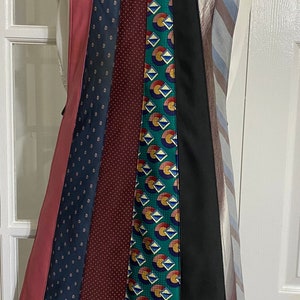 May include: A pink, blue, green, burgundy, and black tie apron. The apron is made from a variety of patterned ties.
