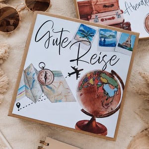 K&ouml;nnte beinhalten: Eine quadratische Geschenkbox mit dem deutschen Text "Gute Reise" und Illustrationen eines Globus, eines Kompasses, einer Landkarte und Polaroidfotos. Eine zweite offene Box zeigt "ES IST Zeit F&Uuml;R EIN NEUES Abenteuer" mit Koffern.