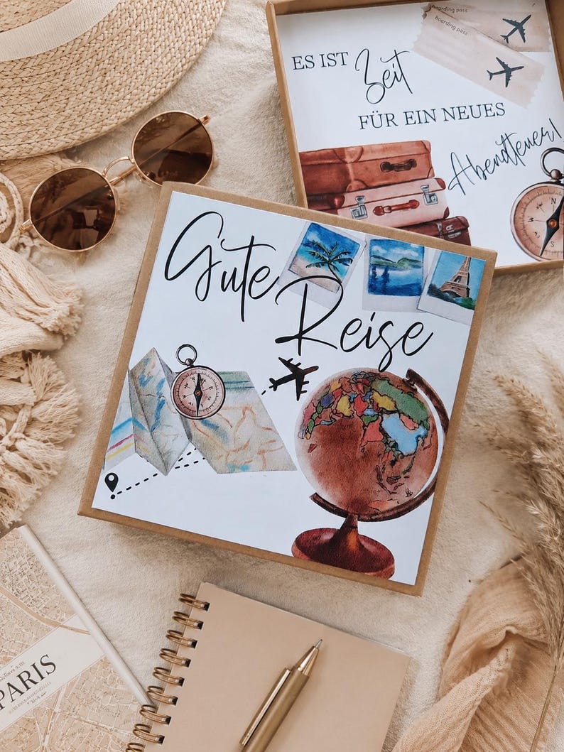 K&ouml;nnte beinhalten: Eine quadratische Geschenkbox mit dem deutschen Text "Gute Reise" und Illustrationen eines Globus, eines Kompasses, einer Landkarte und Polaroidfotos. Eine zweite offene Box zeigt "ES IST Zeit F&Uuml;R EIN NEUES Abenteuer" mit Koffern.