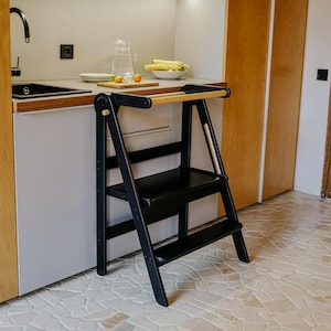 May include: A black wooden step stool with a wooden handrail. The stool has two steps and is in a kitchen setting.