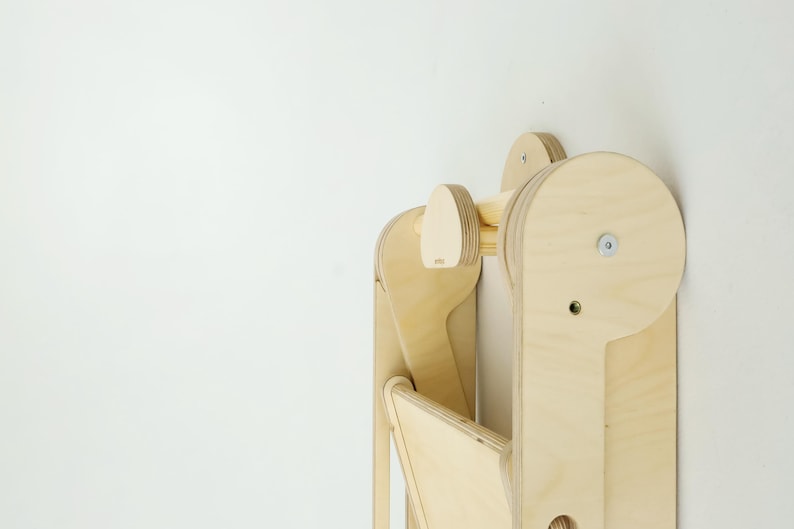 以下が含まれることがあります： 木目がはっきりと見える積層合板で作られた、明るい色の木製折りたたみ式ステップスツール。丸みを帯びたサイドパネル、中央の水平サポートバー、折りたたみ機能のための金属製ボルト機構を備えた構造。