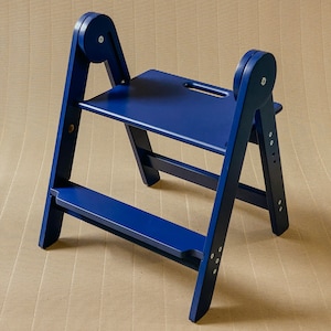 May include: A blue wooden step stool with a small seat and a footrest. The stool has a ladder-like design with rounded supports on the sides. The stool is painted in a solid, vibrant blue color.