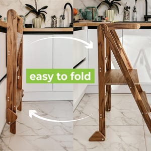 May include: A wooden step stool with a brown finish. The stool is folded up against a white cabinet. The stool is easy to fold and unfold. The text "easy to fold" is written on the image.