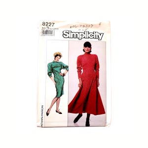 May include: Simplicity sewing pattern number 8227 for a dress. The pattern shows two women wearing dresses, one in green and one in red. The pattern number and Simplicity logo are visible on the front of the package.