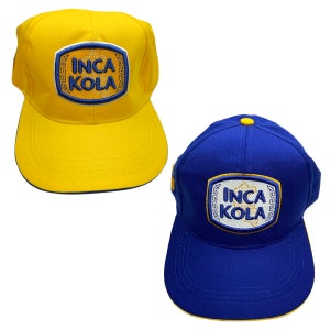 May include: Two baseball caps with the logo "Inca Kola" embroidered on the front. One cap is yellow with a blue brim and the other is blue with a yellow brim.