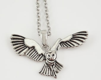 May include: A silver-colored owl pendant with outstretched wings hangs from a delicate chain. The owl's detailed feathers and facial features are visible. The necklace is displayed against a white background, highlighting the jewelry.