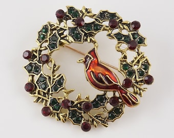 May include: A gold-tone brooch featuring a red cardinal bird perched in a holly wreath with red and green rhinestones.