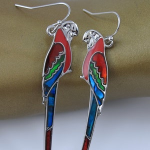 May include: A pair of silver dangle earrings featuring parrot designs with red, green, and blue enamel. The parrots have long tails and are detailed with iridescent accents.