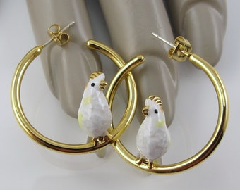 May include: Gold-tone hoop earrings featuring a white and yellow bird charm. The earrings have a polished finish and a post back closure. The bird charms have a detailed design, adding a unique touch to the jewelry.