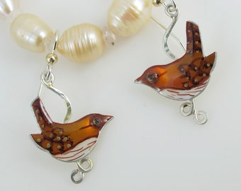 May include: A pair of bird-shaped earrings with a pearl necklace. The earrings feature a brown and white enamel design with silver-tone hooks. The necklace is made of cream-colored pearls.