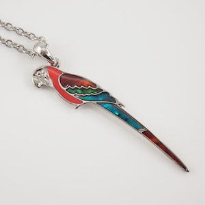 May include: A silver chain necklace with a parrot pendant. The parrot is made of metal and has red, green, and blue enamel.