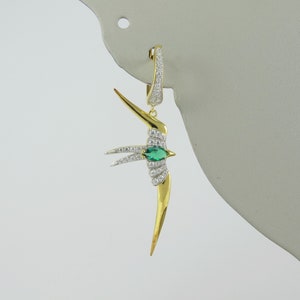 May include: Gold tone dangle earring featuring a stylized bird design with a green gemstone eye and clear crystal accents.