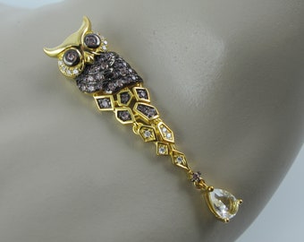 May include: A gold and black owl pendant featuring clear and purple gemstones. The owl is detailed with a textured finish and has a teardrop-shaped gemstone hanging from the bottom.