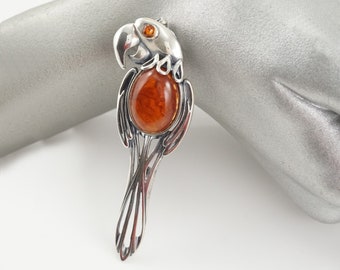 May include: A silver parrot brooch with an amber gemstone. The parrot is detailed with intricate designs and has a round amber stone in the center of its chest.