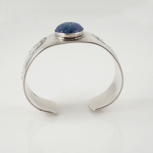May include: A silver cuff bracelet with a blue and green stone set in the center. The bracelet has a textured design.