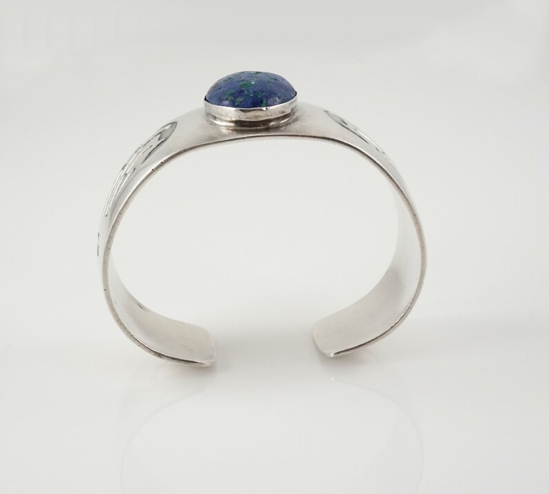 May include: A silver cuff bracelet with a blue and green stone set in the center. The bracelet has a textured design.