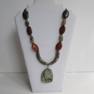 May include: A multi-colored stone necklace with a silver pendant featuring a carved bird design. The necklace features brown, green, and purple stones.