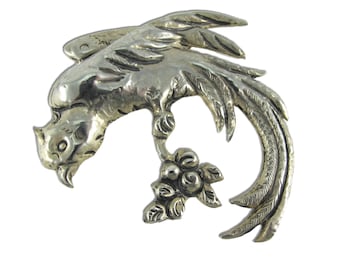 May include: A silver pendant in the shape of a bird with a detailed design. The bird is perched on a branch with berries.