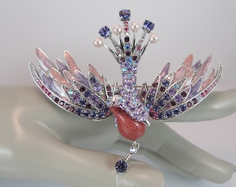 May include: A silver and purple jeweled bird brooch with pink enamel wings and a dangling pearl and crystal drop.