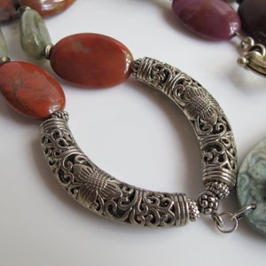 May include: A silver necklace with a decorative floral design and red, green, and purple gemstone beads.