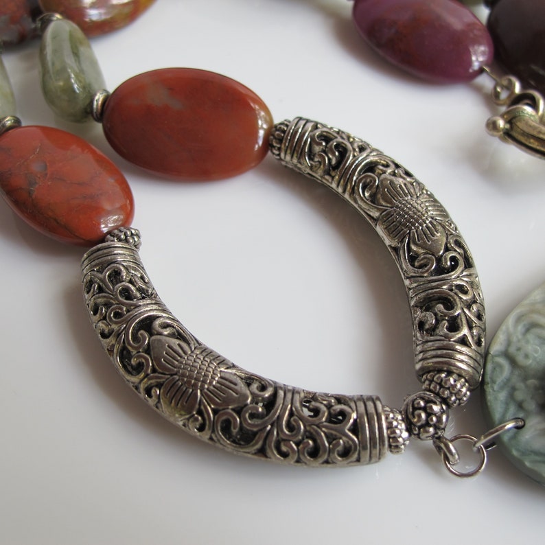 May include: A silver necklace with a decorative floral design and red, green, and purple gemstone beads.