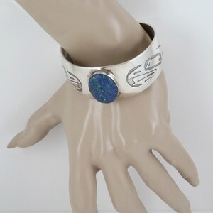 May include: A silver cuff bracelet with a blue stone set in the center. The bracelet is decorated with a carved design.