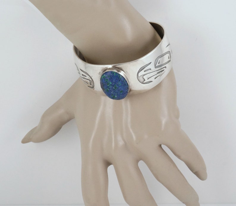 May include: A silver cuff bracelet with a blue stone set in the center. The bracelet is decorated with a carved design.