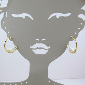 May include: Gold-tone hoop earrings featuring a white bird design with iridescent accents. The bird has a yellow crown. The earrings are displayed on a gray mannequin head.