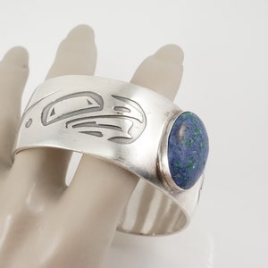 May include: Silver cuff bracelet with a blue and green stone and a carved design.