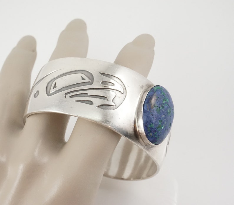 May include: Silver cuff bracelet with a blue and green stone and a carved design.