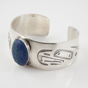 May include: A silver cuff bracelet with a blue and green stone set in the center. The bracelet is decorated with a carved design.