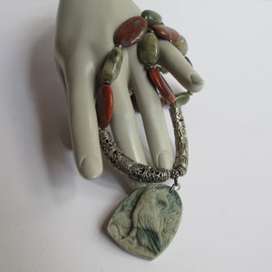 May include: A silver necklace with a carved green stone raven pendant and a multi-colored stone beaded chain.