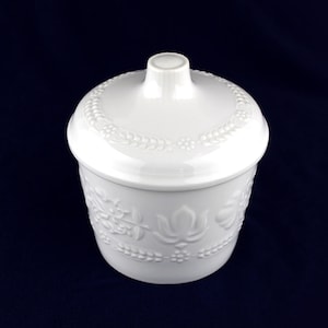 May include: White ceramic jar with a lid, featuring an embossed floral design. The jar has a round shape and a smooth, glossy finish.